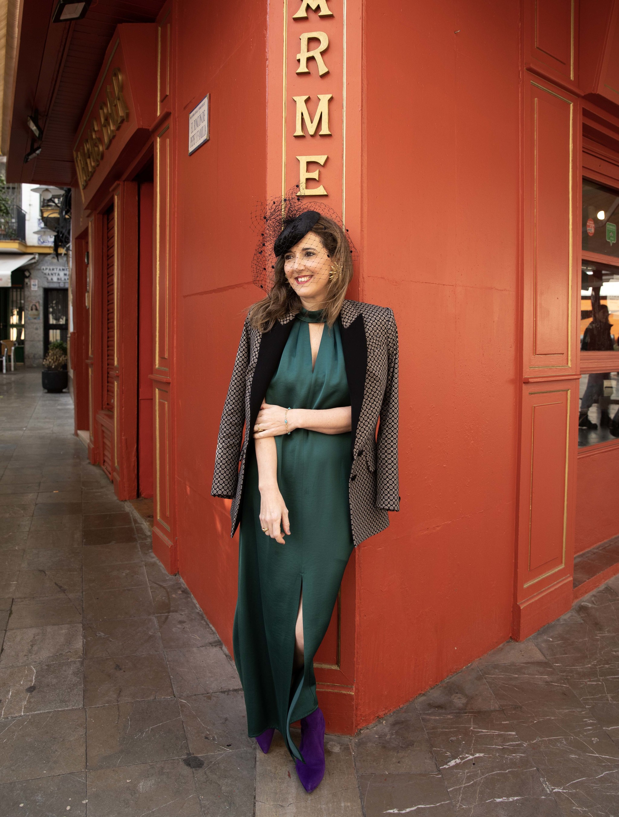 Ana García, diseñadora de Cherubina con vestido satinado verde, chaqueta  estampada y uno de sus tocados.