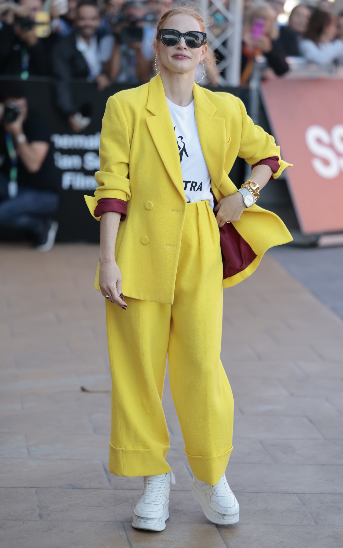 Jessica Chastain con traje de chaqueta amarillo con camiseta reivindicativa.