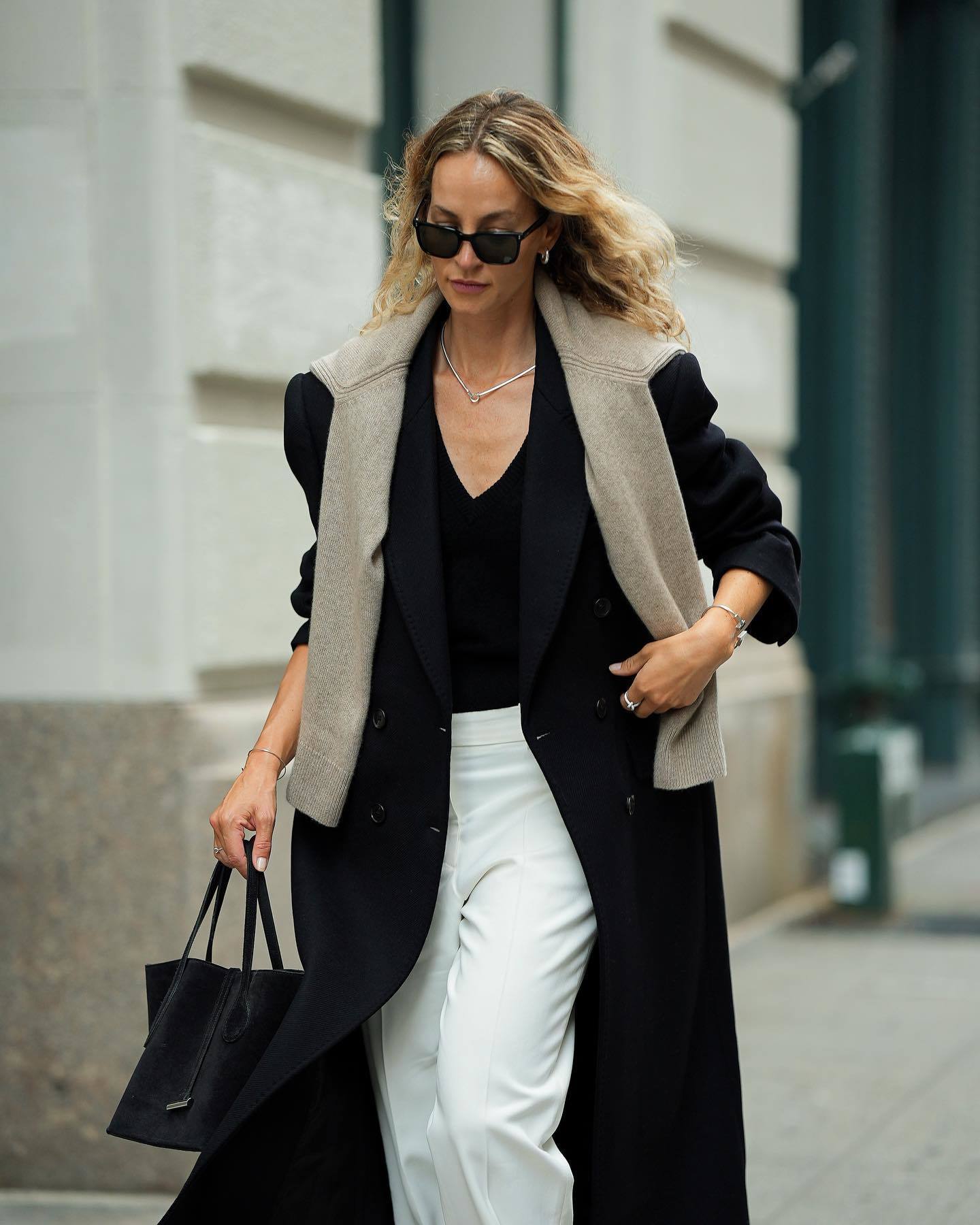 Look de camiseta negra con pantalón blanco y jersey color piedra con abrigo negro.