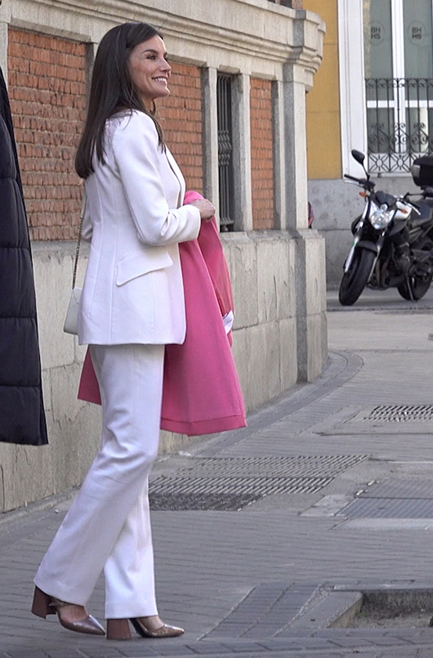 La reina Letizia con sastre blanco, abrigo rosa y zapato color beige.